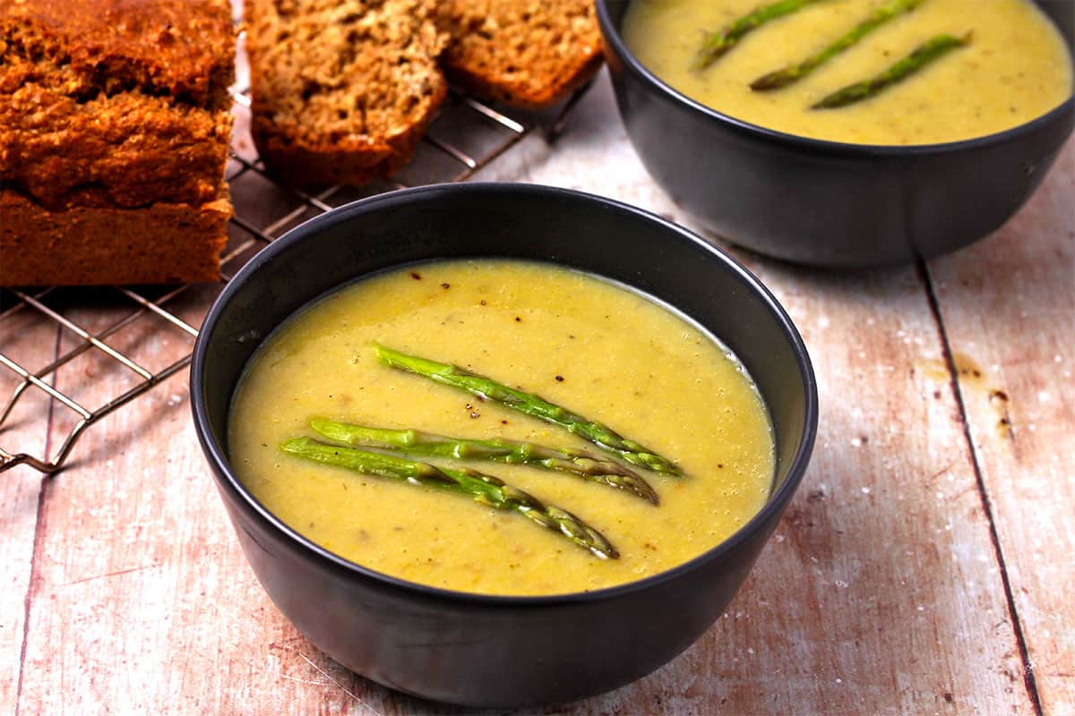 Bowls of creamy asparagus soup with asparagus spears on top.