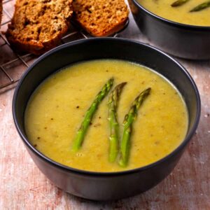 Creamy vegan asparagus soup in a black bowl with asparagus spears on top.