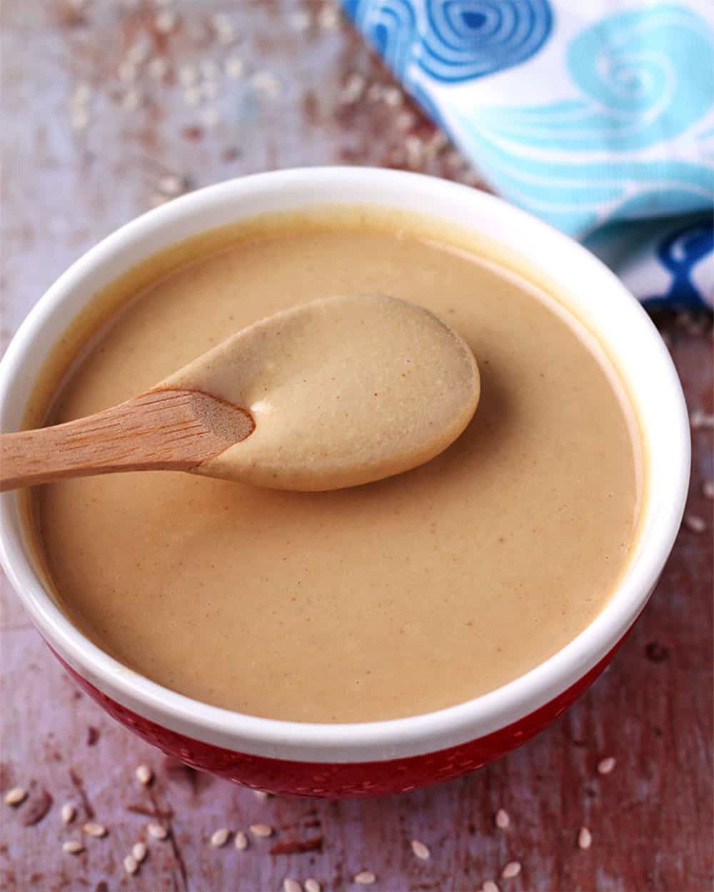 Creamy tahini in a small red bowl with a white brim and a little wooden spoon in it.