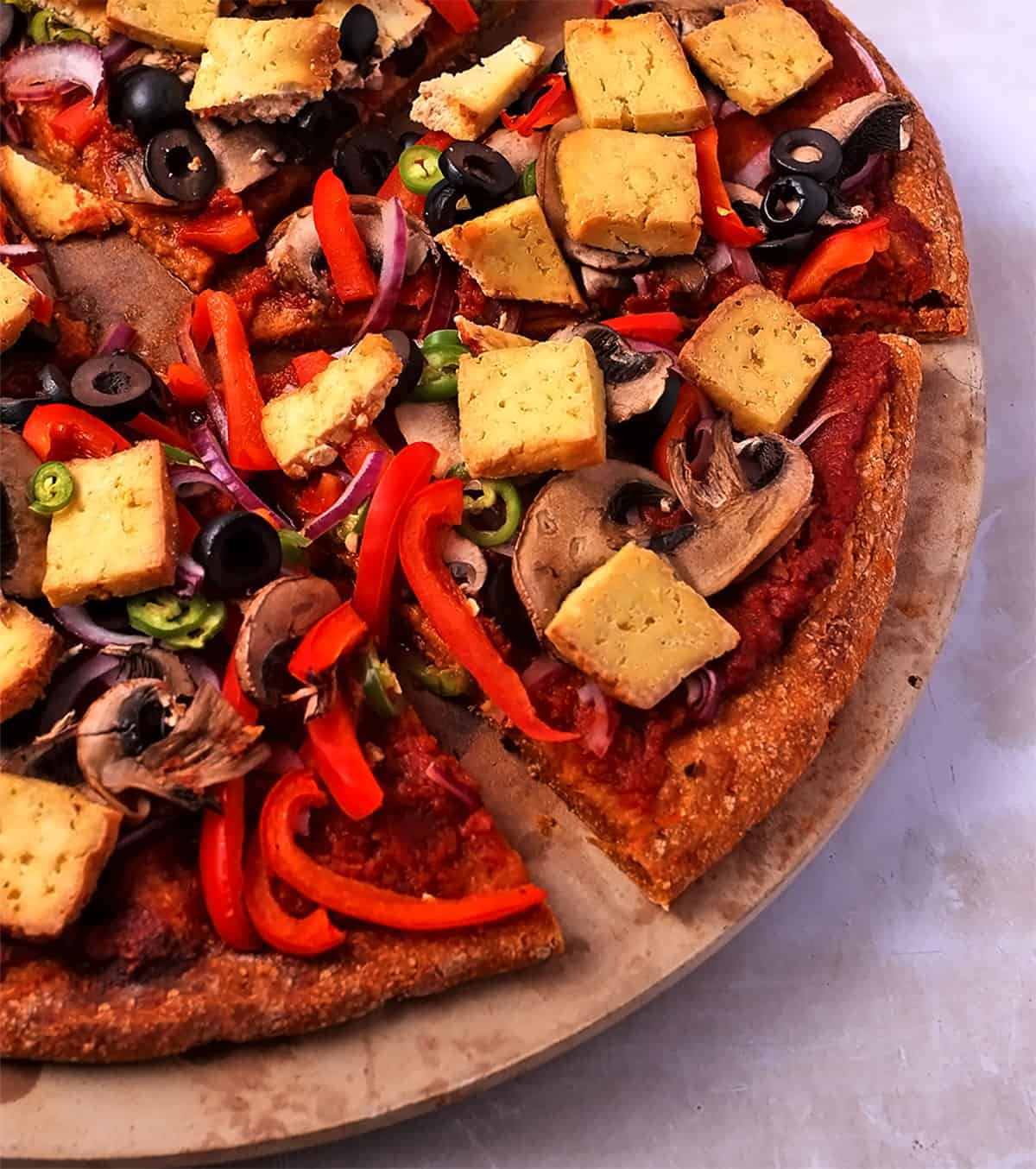 Pizza with sweet potato crust, vegetables, and tofu on a pizza stone.