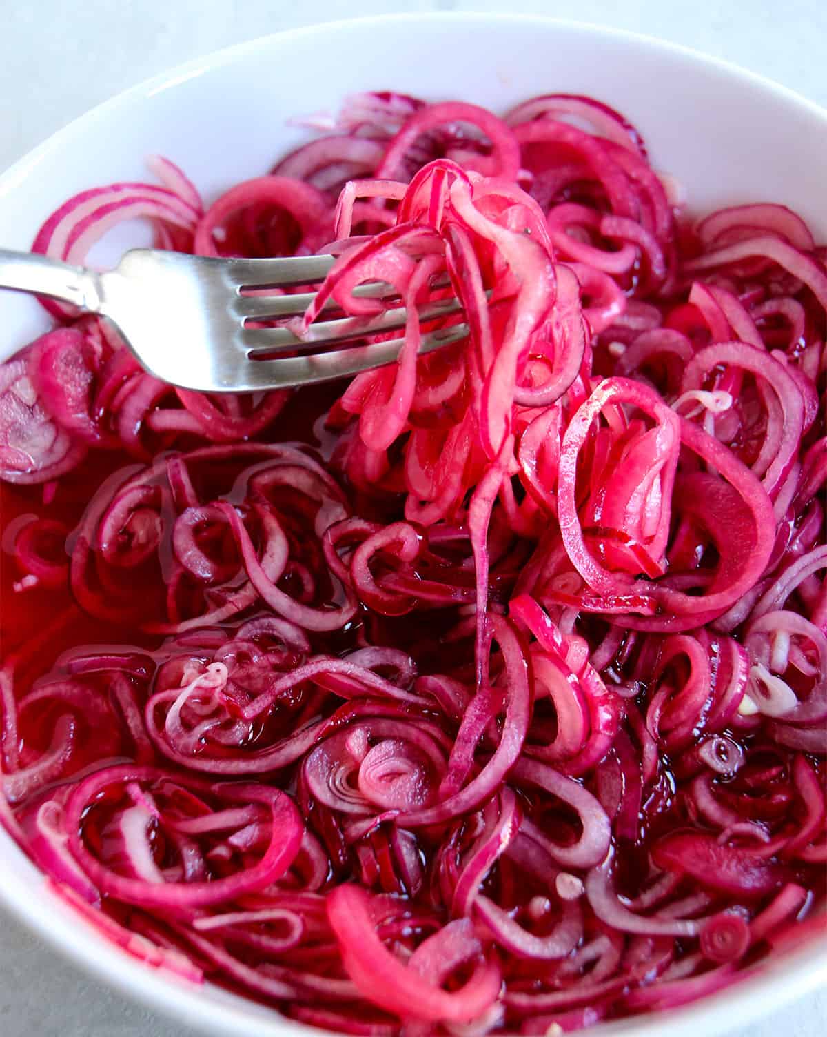 A fork lifts quick pickled red onions from a bowl.