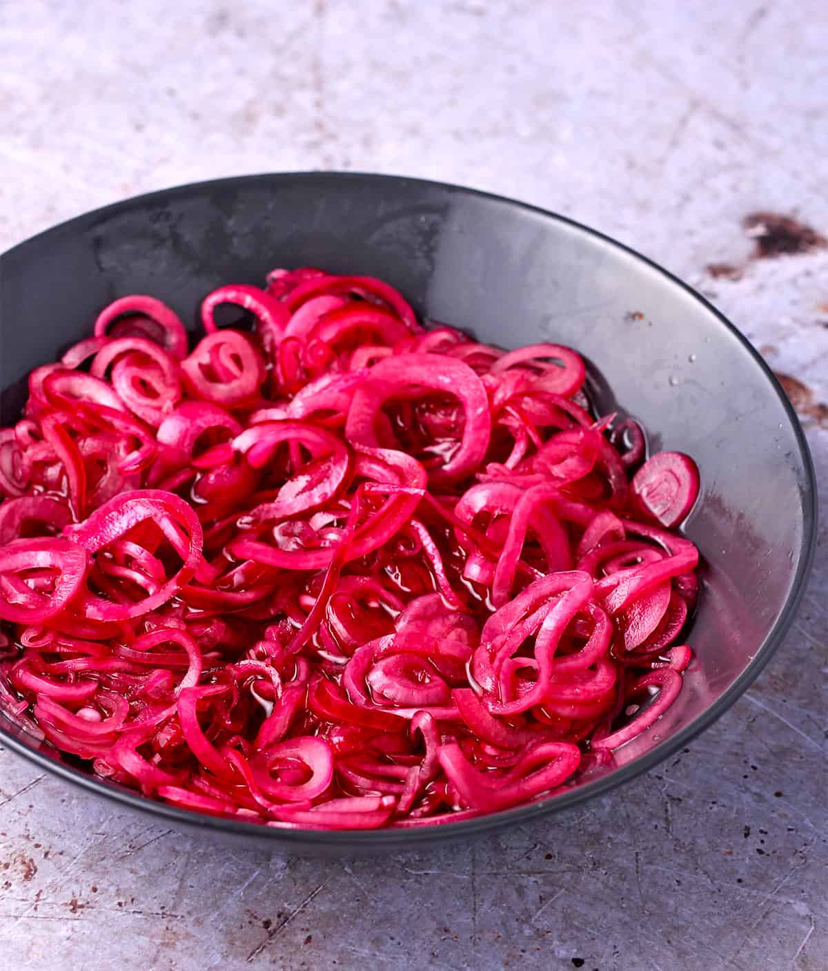 Quick pickled red onion rings in a black bowl.