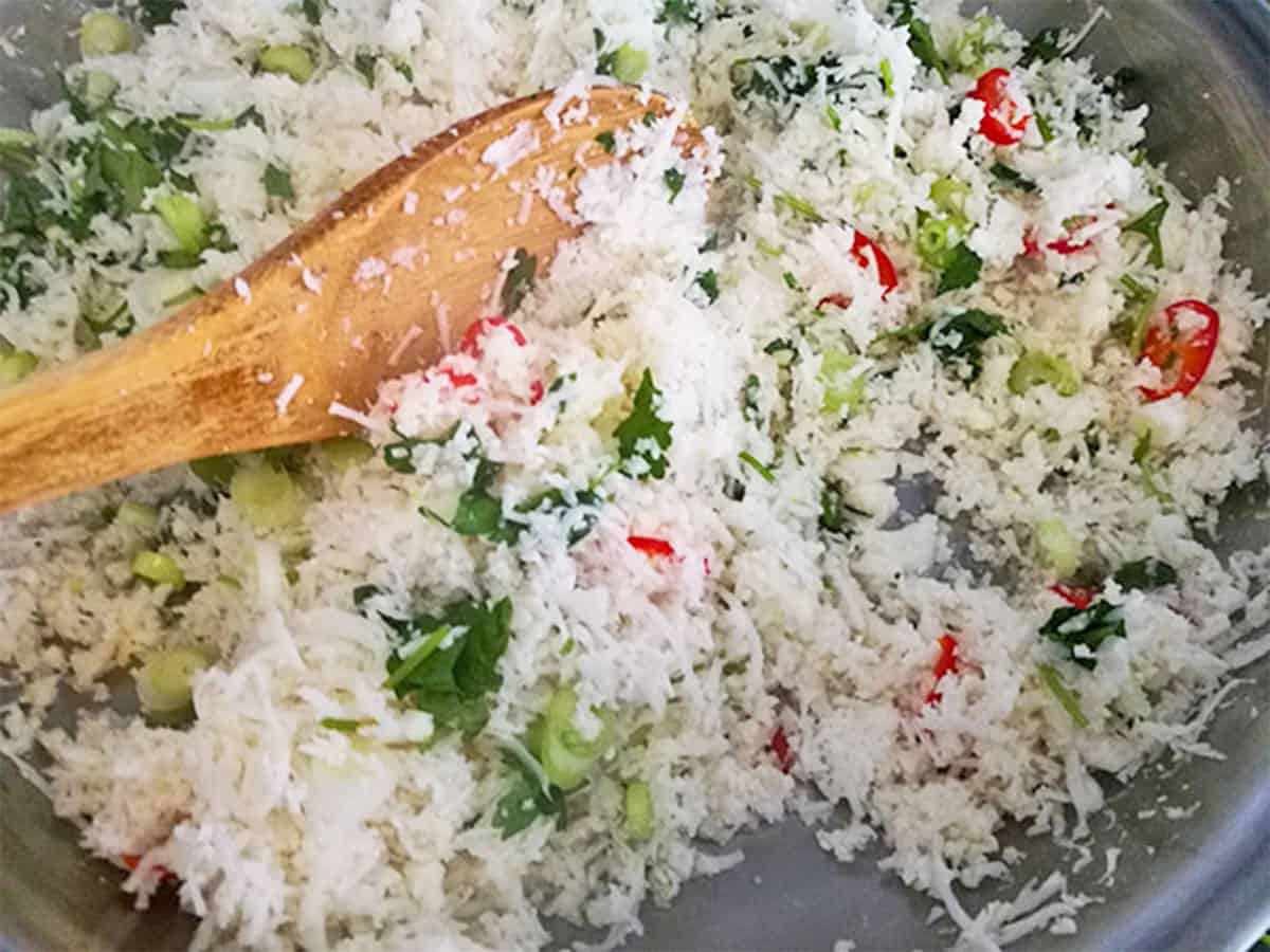 Cauliflower rice with cilantro, scallions, and red chili is stirred in a pan.