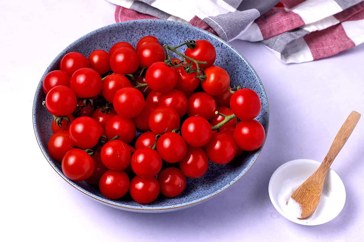 A bowl of fresh, whole cherry tomatoes and a small bowl of salt.