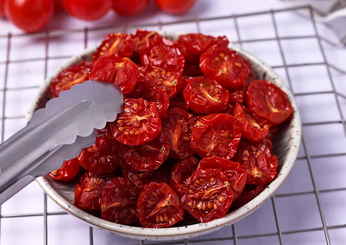 Baked sun-dried tomatoes are grabbed with tongs.