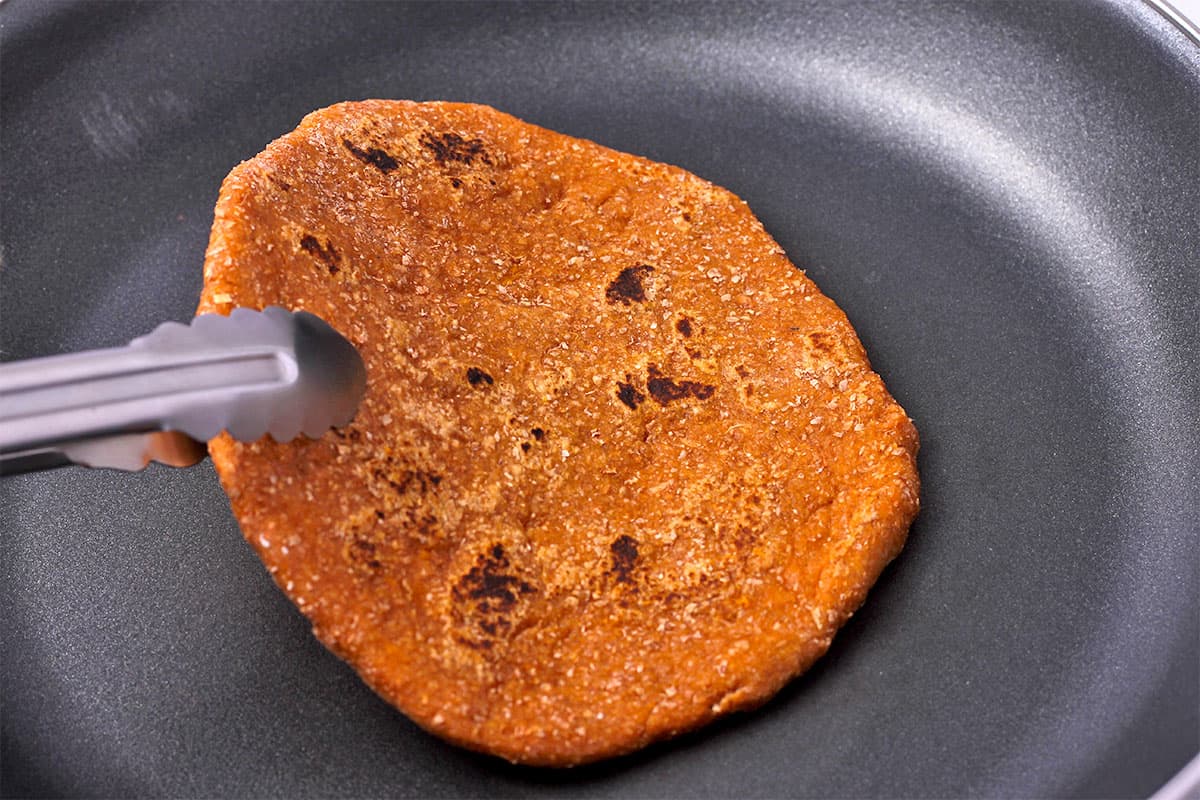 A sweet potato flatbread is flipped in a frying pan.