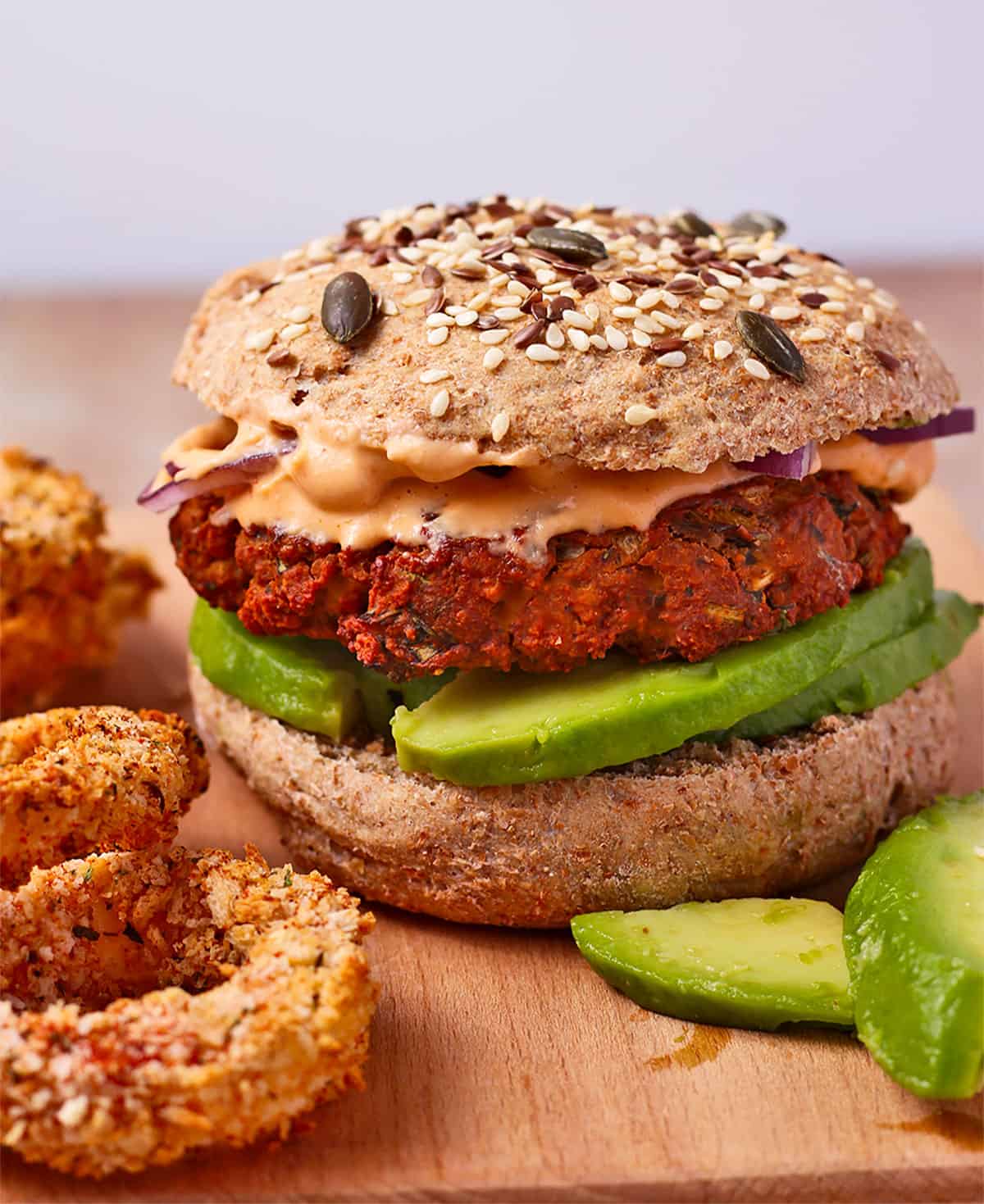 A tofu burger with avocado, onion, and sriracha mayo in a bun.