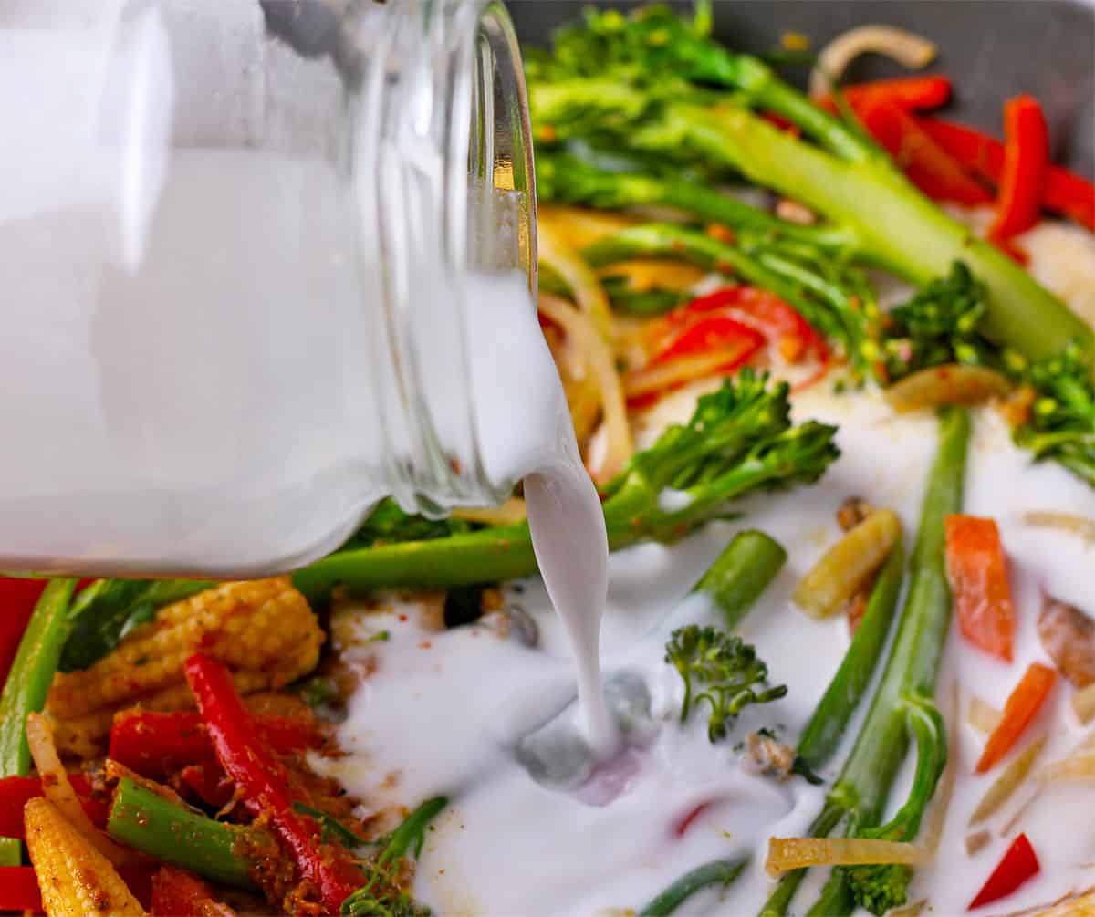 Coconut milk is poured over vegetables for Thai curry.