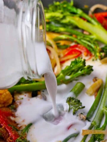 Coconut milk is poured over cooked vegetables.