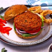 A sweet potato and chickpea burger patty is placed on a bun with lettuce, onion, and tomato.