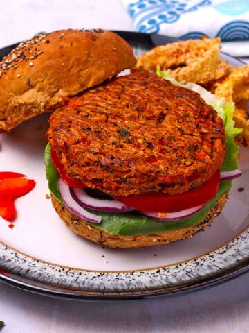 A sweet potato and chickpea burger patty is placed on a bun with lettuce, onion, and tomato.