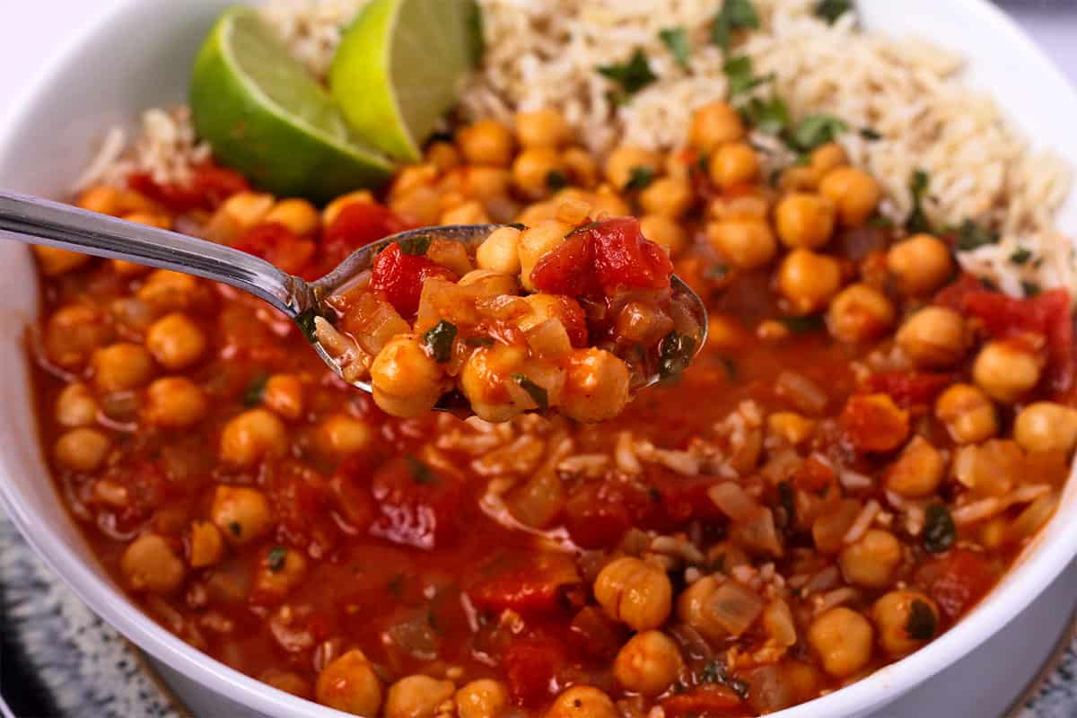 Chickpea coconut curry is lifted in a spoon over a bowl.