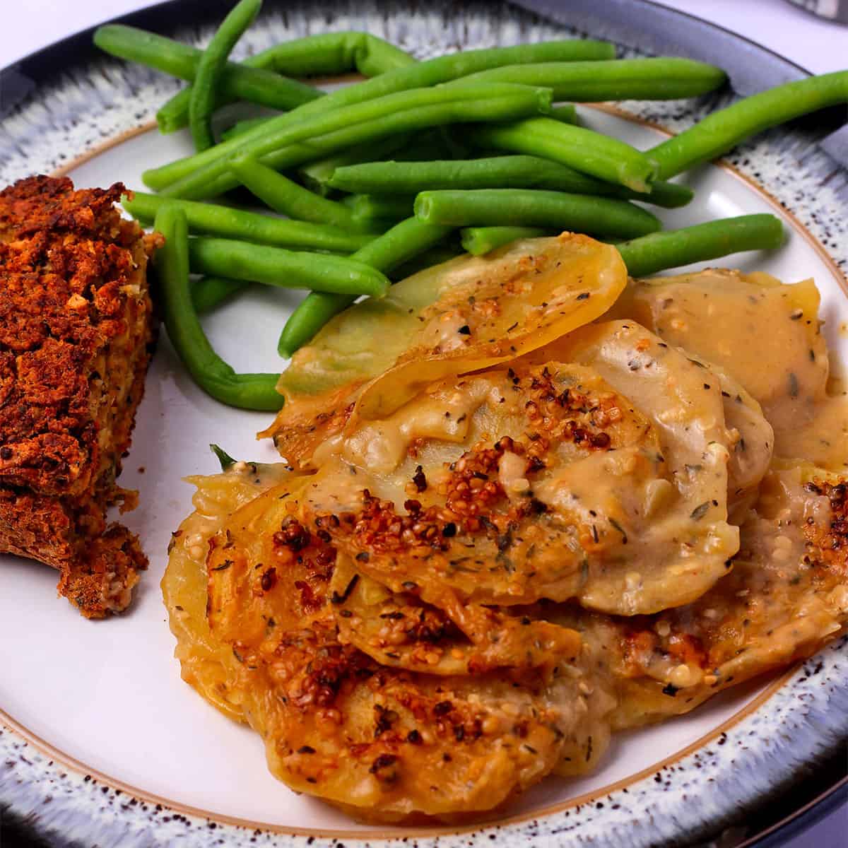 A plate with vegan scalloped potatoes, green beans, and nut loaf.