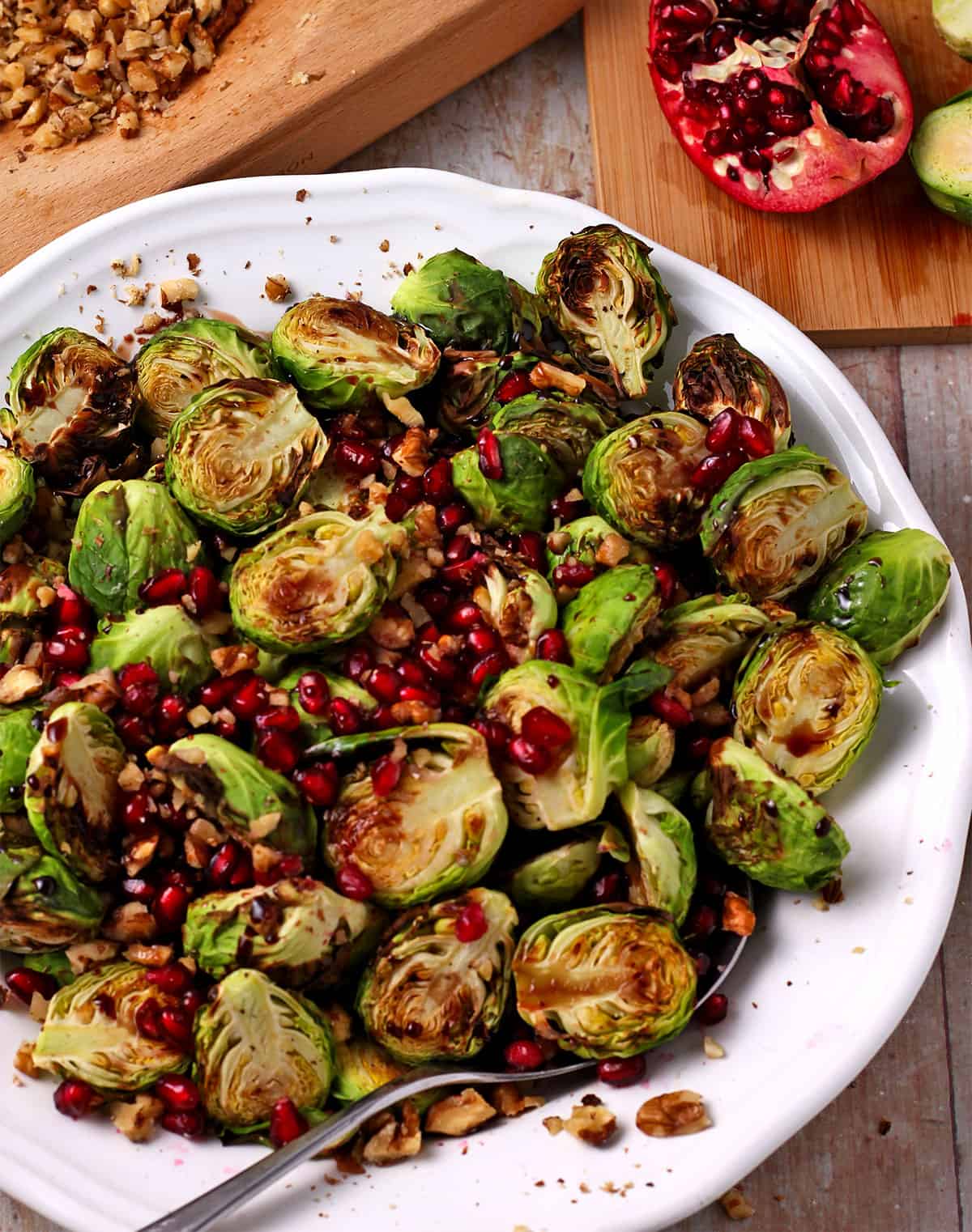 A bowl of brussels sprouts with pomegranate seeds, walnuts, and a spoon.