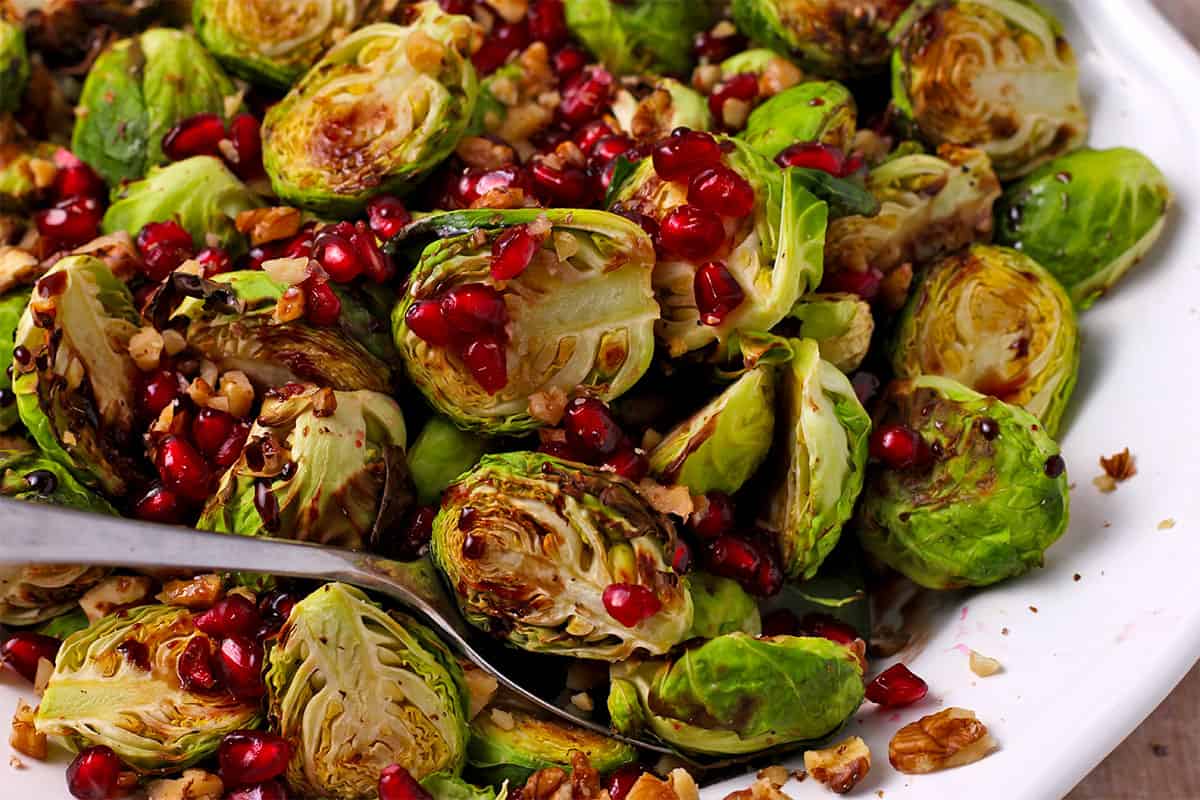 A brussels sprout half with pomegranate seeds, walnuts, and pomegranate molasses on a spoon.