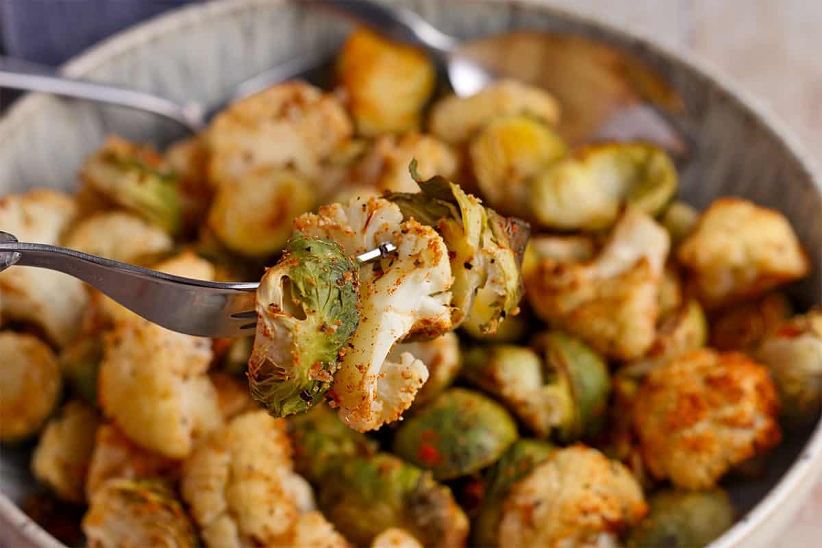 A roasted brussels sprout and cauliflower floret pierced with a fork.