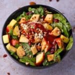A bowl of apple cranberry salad with spinach, almonds, and cranberry balsamic dressing.