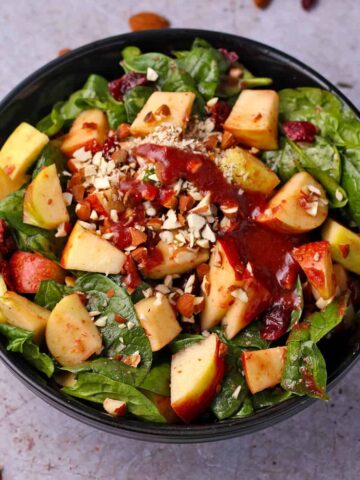 A bowl of apple cranberry salad with spinach, almonds, and cranberry balsamic dressing.