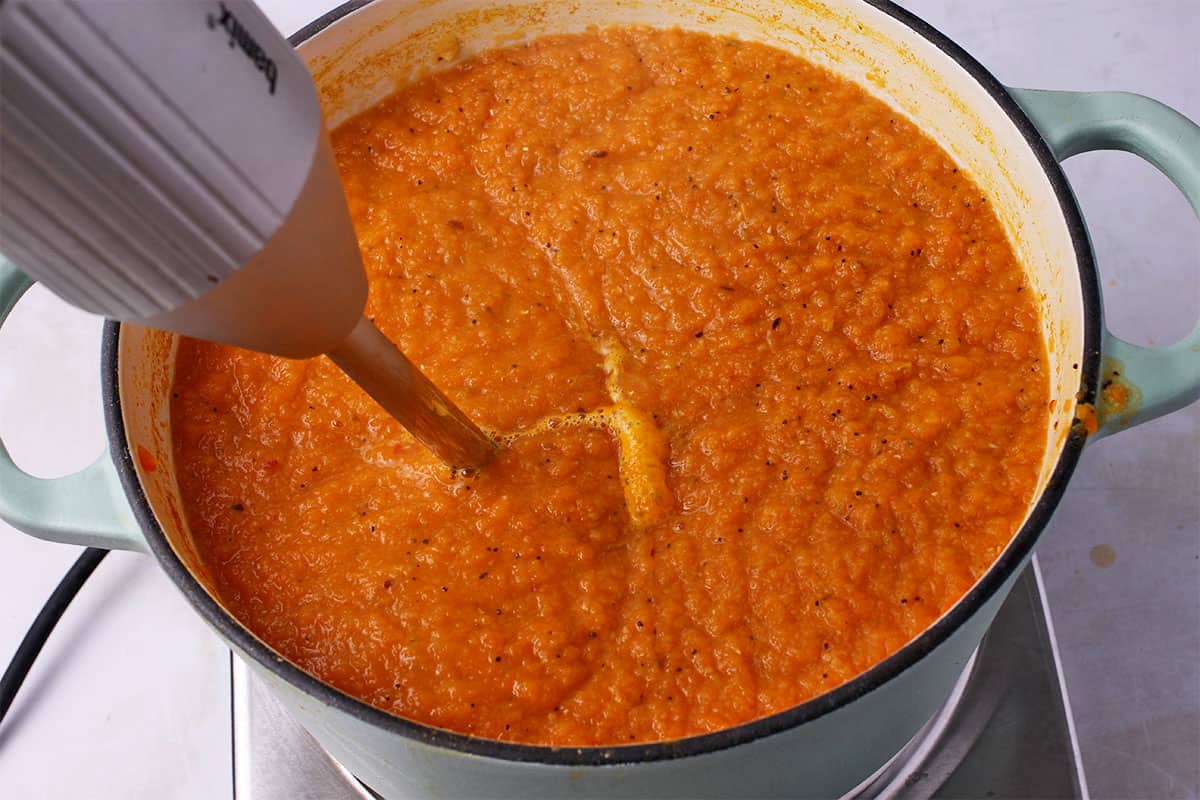 Carrot lentil soup is pureed with an immersion blender.