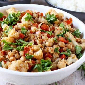 Cauliflower and chickpea curry with tomatoes and cilantro in a white bowl.