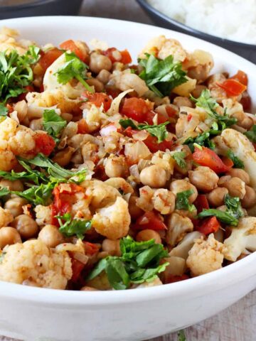Cauliflower and chickpea curry with tomatoes and cilantro in a white bowl.