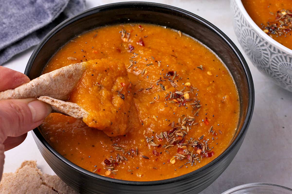 Pita bread is dipped into carrot and red lentil soup with cumin seeds, mustard seeds, and chili flakes.