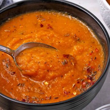 A spoon is dipped into a bowl of spiced carrot and lentil soup.