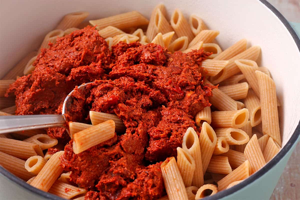 Red pesto is mixed with cooked pasta.