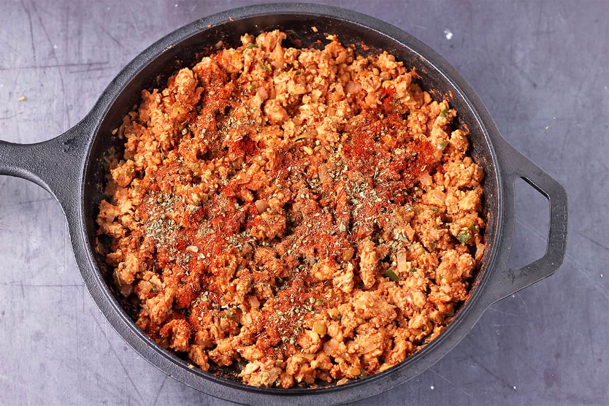 Spices are sprinkled over crumbled tempeh with onion and jalapenos.