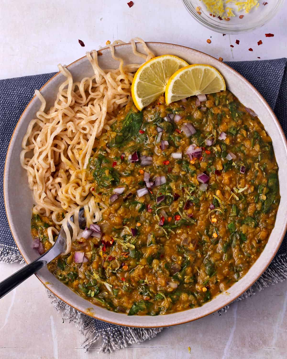 Curry with spinach and lentils in a bowl with noodles and a fork.