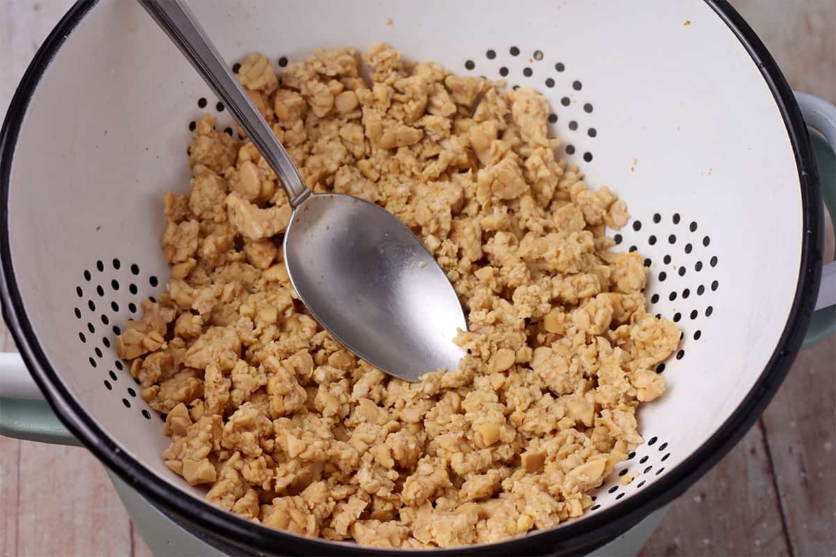 Simmered tempeh crumbles are pressed in a colander.