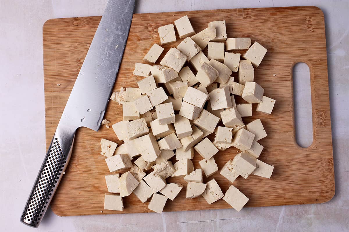 Tofu cubes on a cutting board with a knife.