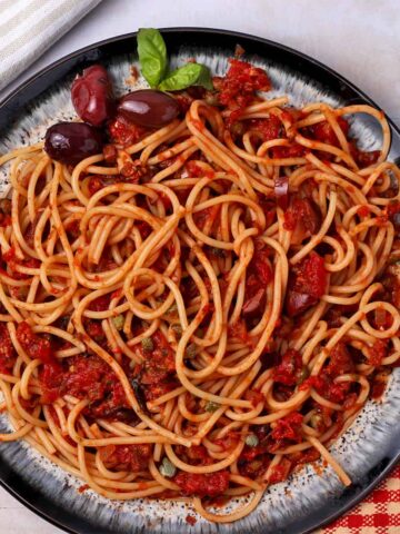 Spaghetti puttanesca with olives and capers on a plate.