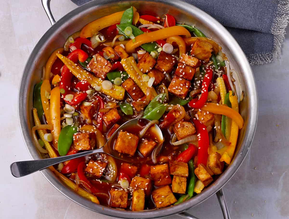 Sweet and sour tofu with vegetables in a pan with a spoon.