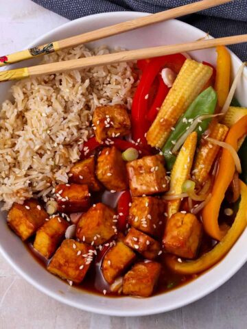 A bowl of sweet and sour tofu with rice and vegetables.