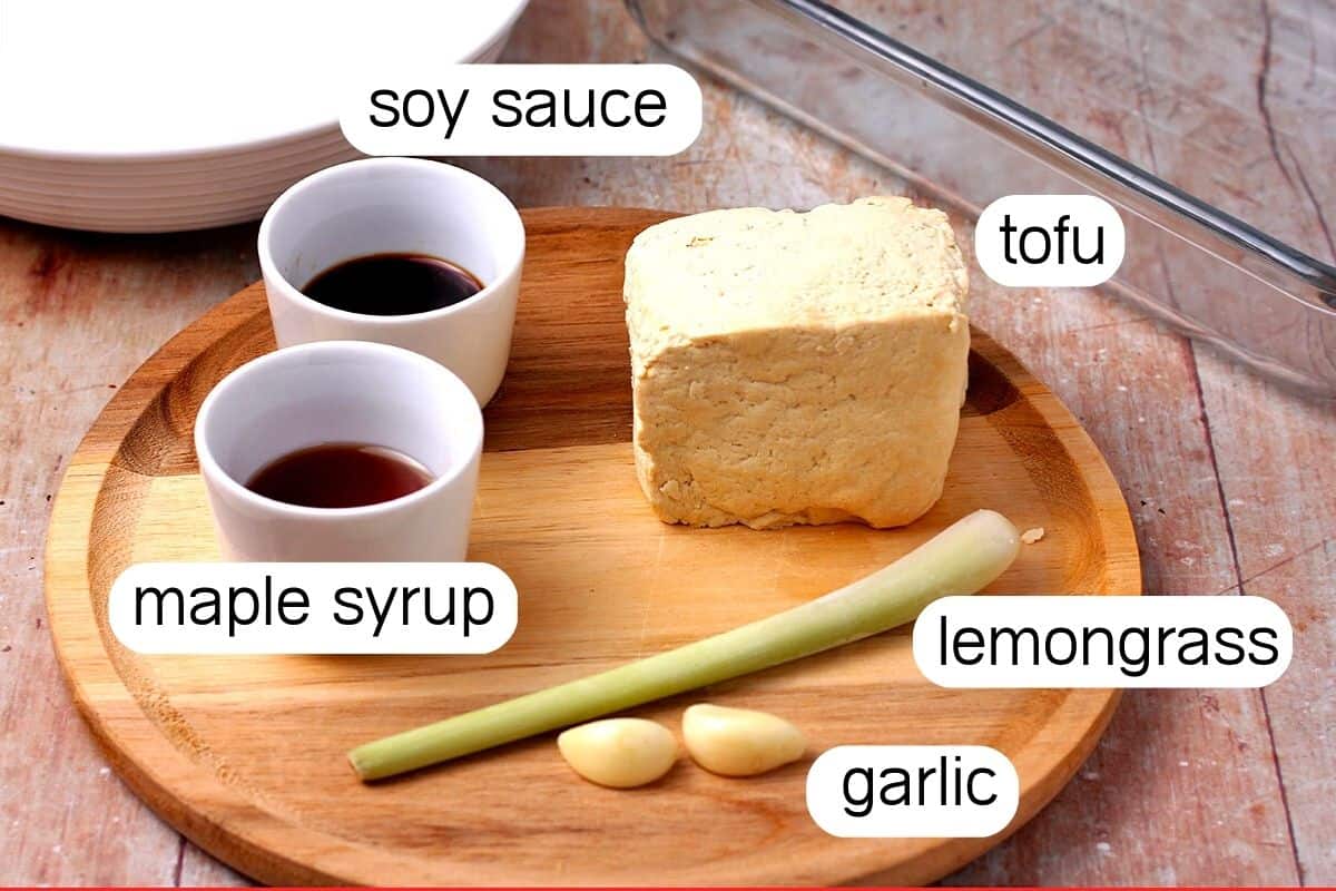 The ingredients for lemongrass tofu on a round wooden plate with ingredient labels.