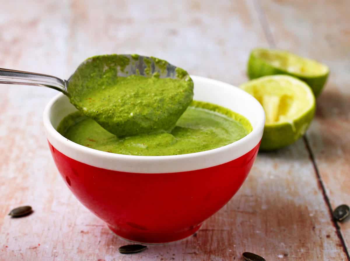 A red bowl with green cilantro lime dressing with a spoon.