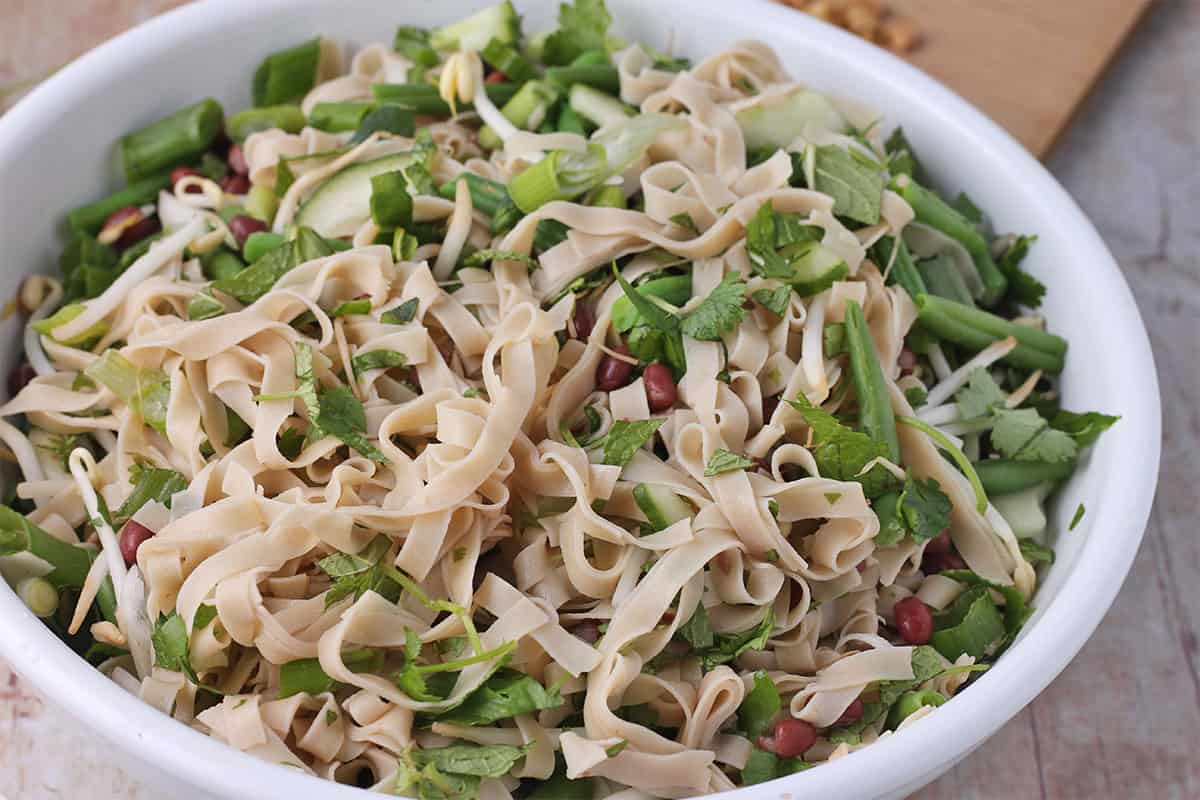 Cooked rice noodles are added to a salad of greens and beans.