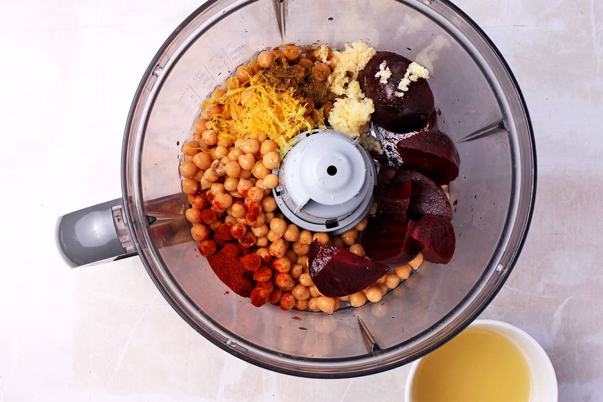 Beets, garlic, chickpeas, lemon zest, and spices are added to a food processor.