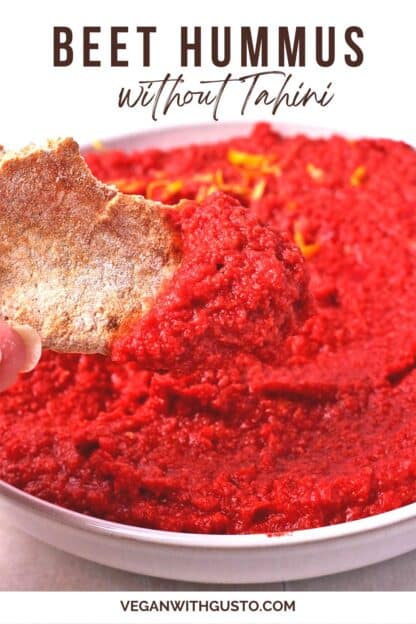 A pita bread sliced is dipped into a bowl of beet hummus.