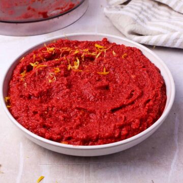 Beet hummus without tahini in a white bowl with lemon zest on top.