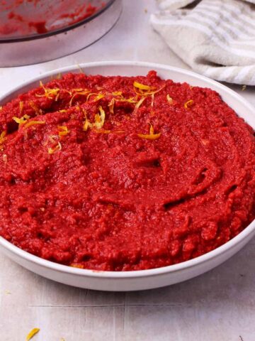 Beet hummus without tahini in a white bowl with lemon zest on top.