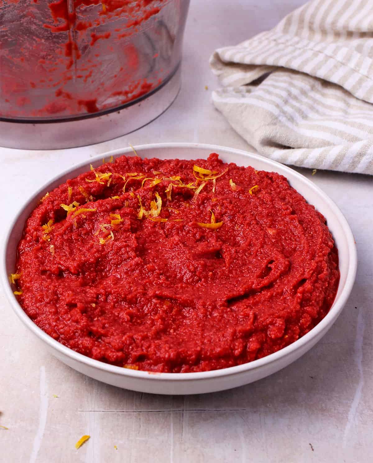 Blended beet hummus with lemon zest in a white bowl.
