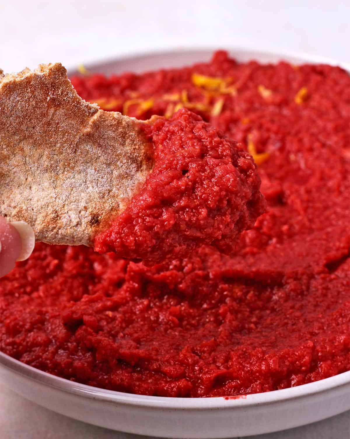 Pita bread is dipped into a bowl of beet hummus.