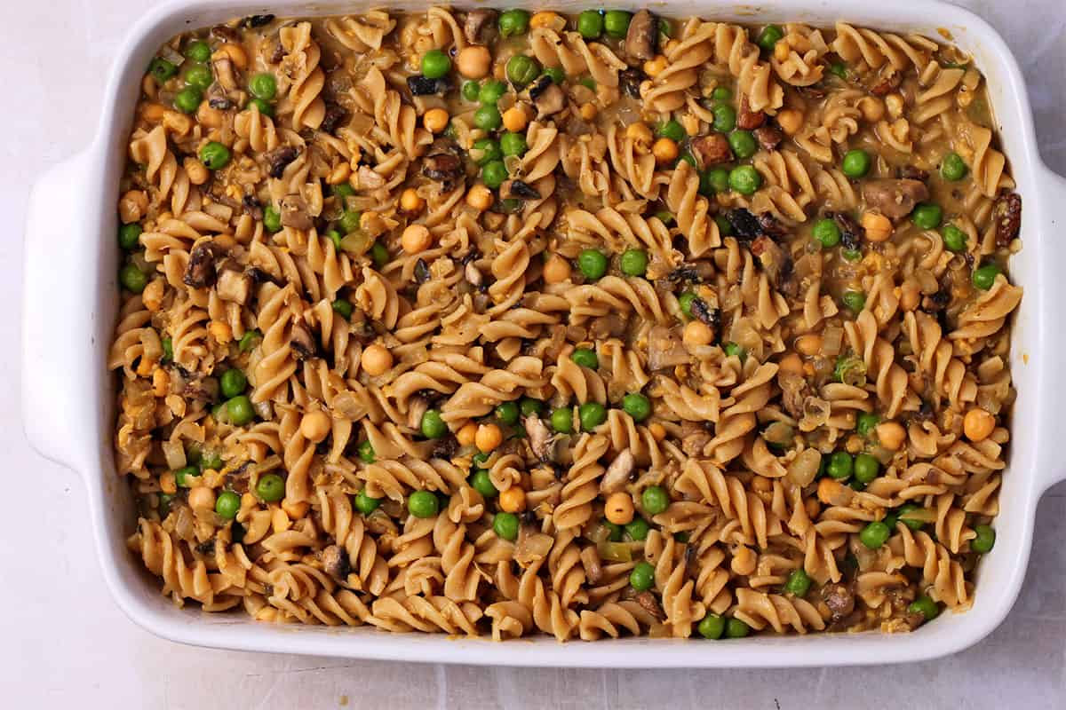 A casserole dish filled with cooked pasta, chickpeas, green peas, and mushrooms.