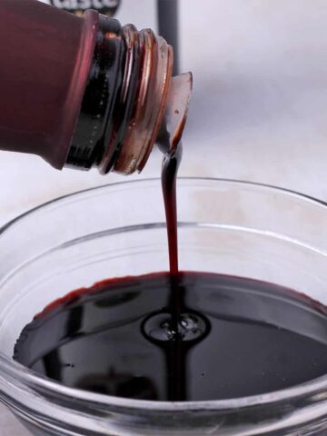 A bottle of pomegranate molasses is poured into a small glass dish.