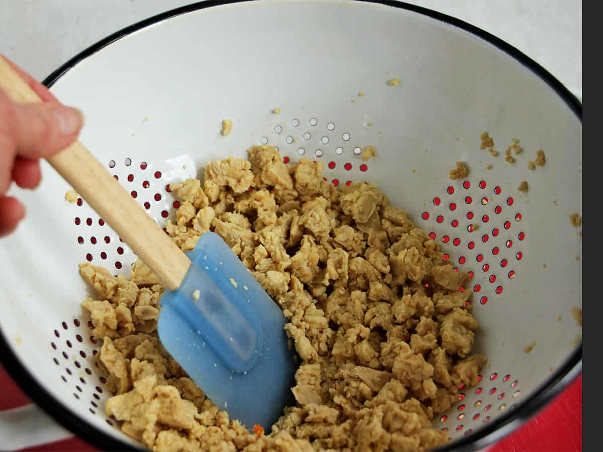 Tempeh crumbles are pressed in a colander.