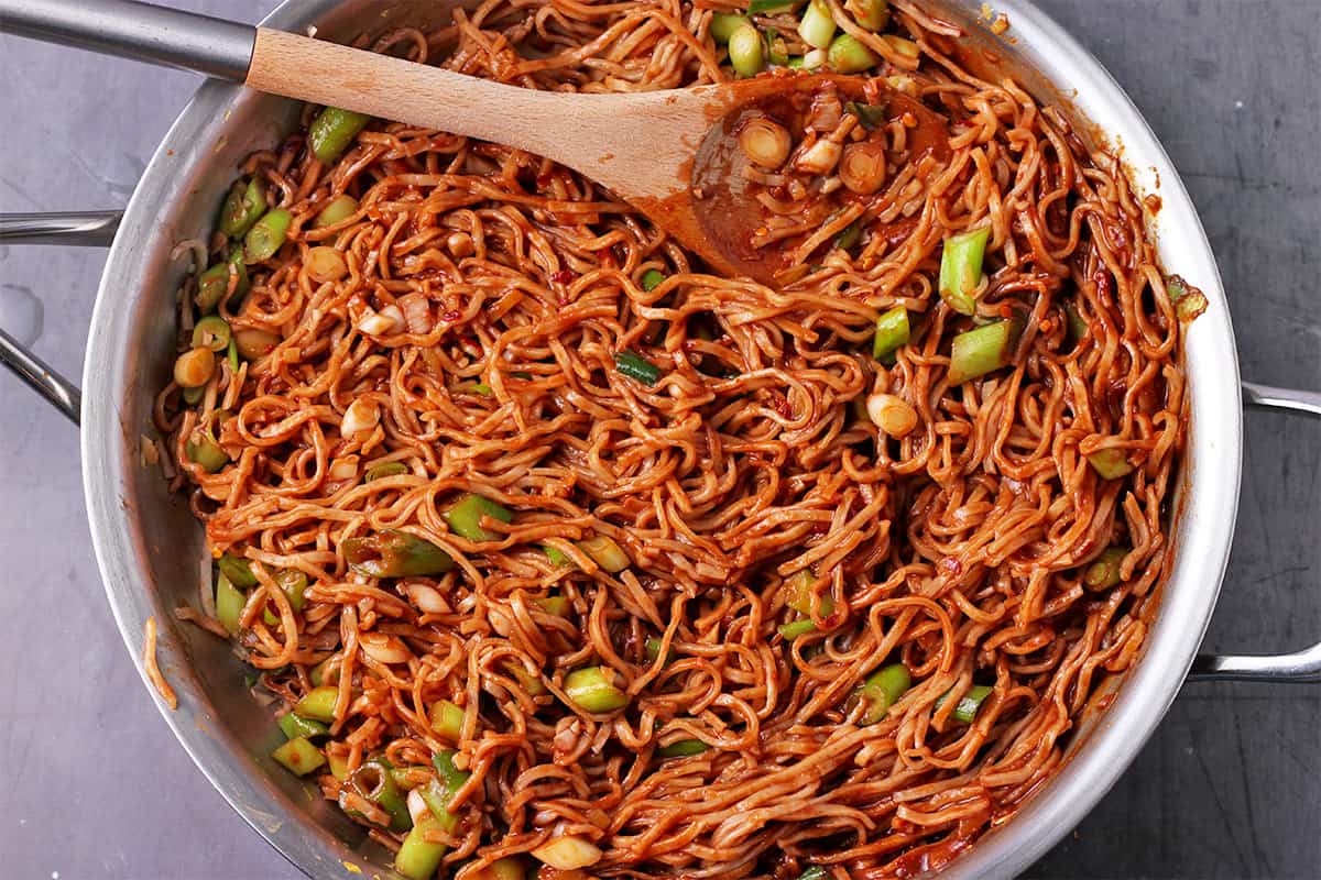 Cooked noodles are mixed with green onions and sauce.