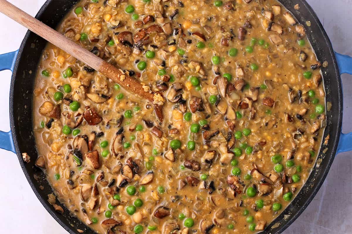 A skillet with cooked mushrooms, green peas, and chickpeas in sauce.