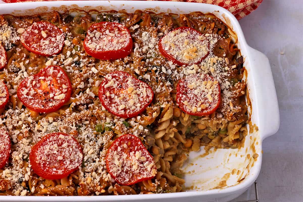 Vegan tuna casserole with sliced tomatoes and breadcrumbs in a white casserole dish with a slice of casserole removed.